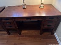 Front view of the wooden desk showcasing the seven drawers and the desktop surface with two lamps placed on top.