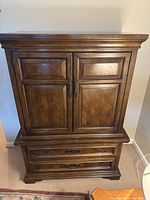 Full front view of the wooden armoire showing the upper cabinet doors and lower drawers in a rural English style by Dixie Furniture Company.