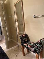 Photo of bathroom accessories showing a floral upholstered stool, metal towel rack, and wall mirror.