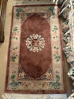 Top-down view of rectangular carpet showing floral central pattern and border with floral and geometric designs in rust brown and cream colors.