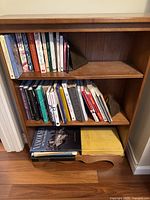 Front view of wooden bookcase filled with books showing three shelves and bottom shelf with curved detail.
