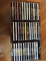 Top view of three rows of music CDs arranged tightly in a black case or tray, showing multi-colored spines with text and barcode stickers visible.