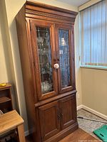 Full view of tall wooden china cabinet with leaded glass doors on upper section, lower solid wood doors and crown molding.