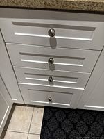 Four white kitchen drawers with silver knobs installed under granite countertop.