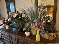 Wide view of all faux flower arrangements displayed on wooden cabinet including various vases and pots