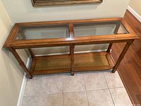 Front view of wooden hall table with glass top and lower wooden shelf against a beige wall on tiled flooring.
