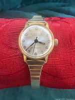 Front view of Kienzle Madame ladies mechanical wristwatch, gold-tone case, white dial with Arabic numerals, black hands, and brand markings.