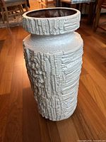 Full front view of off-white/beige ceramic vase on wood floor