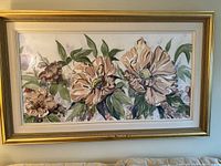 Front view of the framed watercolour painting showing the floral artwork within the ornate gold frame hung on a light blue wall.