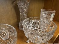 Shelf display of assorted lead crystalware including stacked bowls, a tall vase, and small crystal figurines showing pinwheel cut patterns