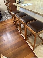 Side angle view of four stools lined up under kitchen counter, showing frame and seat profile