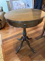 Wooden drum style table with round top, four curved legs, and brass-capped feet on hardwood floor.