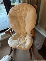 Oak rocking chair with beige padded seat cushion in natural lighting near window.