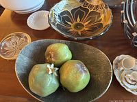 Photo of black and gold ceramic bowl, brown and white striped bowl with artificial pears, and clear glass dish.