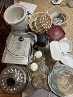 Overview of various kitchen items including ceramic crock, metal bakeware such as bundt pan and egg mold, glass baking dishes, plastic storage containers, insulated thermos, and small bowls.
