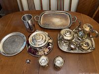 Photo showing silver goblets, serving trays, covered dish, and silver plated tea set on table.