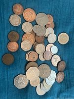 Photo showing spread of various vintage English coins on blue fabric including pennies, two pence, florins and more.