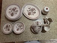 Overview of various dishware pieces including plates, bowls, serving platter, sugar pot, and creamer with floral pattern on countertop.