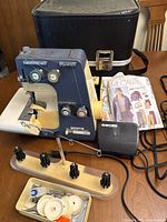 Full view of the White Super Lock 534 serger with foot pedal, threading stand, assorted spools of thread, sewing tools, oil bottle, McCall's sewing patterns, and hard carrying case.