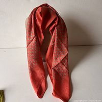Long coral silk scarf with small repeated rounded motifs draped against white background showing texture and details.