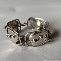 Close-up photo showing the sterling silver bracelet with linked rectangular panels, heart shapes, and spherical accents.
