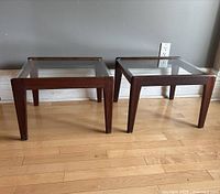 Front view of both teak end tables side by side on hardwood floor under wall outlet.