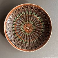 Top view photo showing full circular plate with radiating swirl marblized glaze pattern in multiple earth tones, highlighting intricate handmade pattern and color variation.