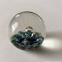 Front view of clear spherical glass paperweight showing blue and green abstract pattern and bubbles inside