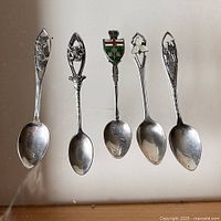 Five antique sterling silver souvenir spoons showing front details including maple leaves, Dogwood flower, enamel shield with Niagara Falls, Trillium, and Mounted Police Calgary.