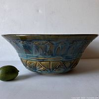 Full side view of the large studio pottery bowl showing blue-green glazed surface and stamped geometric patterns. Lime included for size reference.