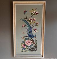 Full front view of the framed vintage hand embroidered silk artwork showing a large bird, flowers, and butterflies on muted background.