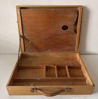 Open wooden paint box showing the interior compartments and slide-in palette with thumb hole.
