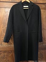 Full front view of black Zara Basic Handmade wool cashmere coat hanging on wooden wall.