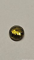 Faceted round cut African sphene gemstone displaying its color and fire under direct light on a plain background.