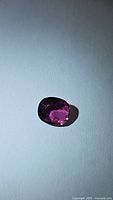 Oval cut pink tourmaline gemstone placed on a white background, showing vivid blossom pink color and facets.