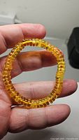 Close-up photo of bracelet held in hand showing translucent golden amber disc beads.
