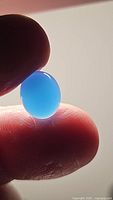 Photo of an oval cabochon icey blue chalcedony gemstone held between fingers showing translucent blue color and smooth polished surface.