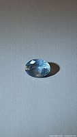 Oval cut natural aquamarine gemstone laid on flat surface showing clarity and blue tone.