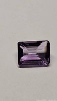 Close-up of natural purple amethyst emerald step cut gemstone showing facets and color uniformity.