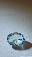 Oval cut aquamarine gemstone placed on a light surface showing reflections and internal facets.