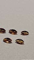 Five marquis cut Madeira citrine gemstones arranged on a flat surface, showing facets and rich amber color.