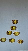 Seven oval cut natural sapphires in bright canary yellow color arranged on white background.