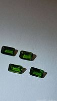 Four emerald cut green chrome diopside gemstones evenly spaced on white background showing clarity and color.
