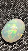 Close-up photo of oval Ethiopian opal cabochon showing bright multicolored play-of-color on a black textured background.