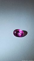 Oval cut natural hot pink topaz gemstone seen from above showing its facets and vibrant pink hue.