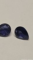 Two natural purple iolite pear cut gemstones shown on a plain light background, focus on color and cut details.
