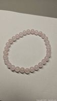 Photo showing the natural rose quartz bracelet laid out in a circular shape on a flat surface with soft lighting highlighting the soft pink color and smooth bead texture.