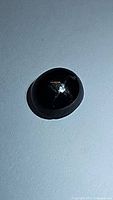 Oval jet black star diopside cabochon gemstone, showing faint 4-ray star effect under lighting