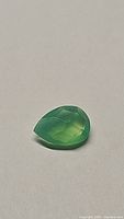 Front angle view of natural vivid green Onyx pear-shaped gemstone showing checkerboard faceted cut.