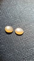 Two natural peach moonstone oval cabochons displayed on textured surface, showing color and translucency under light.